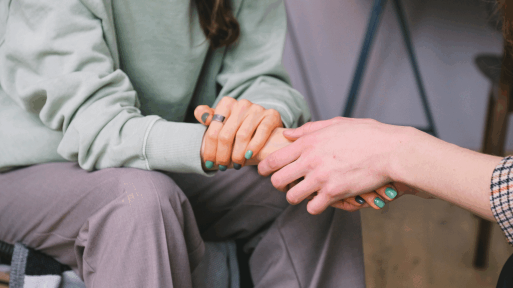 A woman gently holds the hand of another woman, conveying support and connection between them.